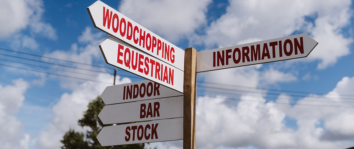 Kumeū Show signpost pointing to woodchopping, equestrian, information, indoor, bar and stock